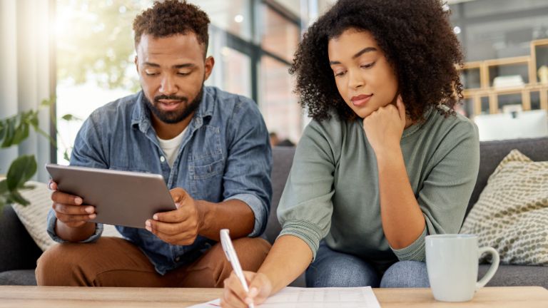 Young mixed race couple going through documents and using a digital tablet at a table together at home