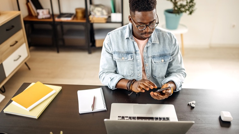 A man seated at a desk checking his cell phone